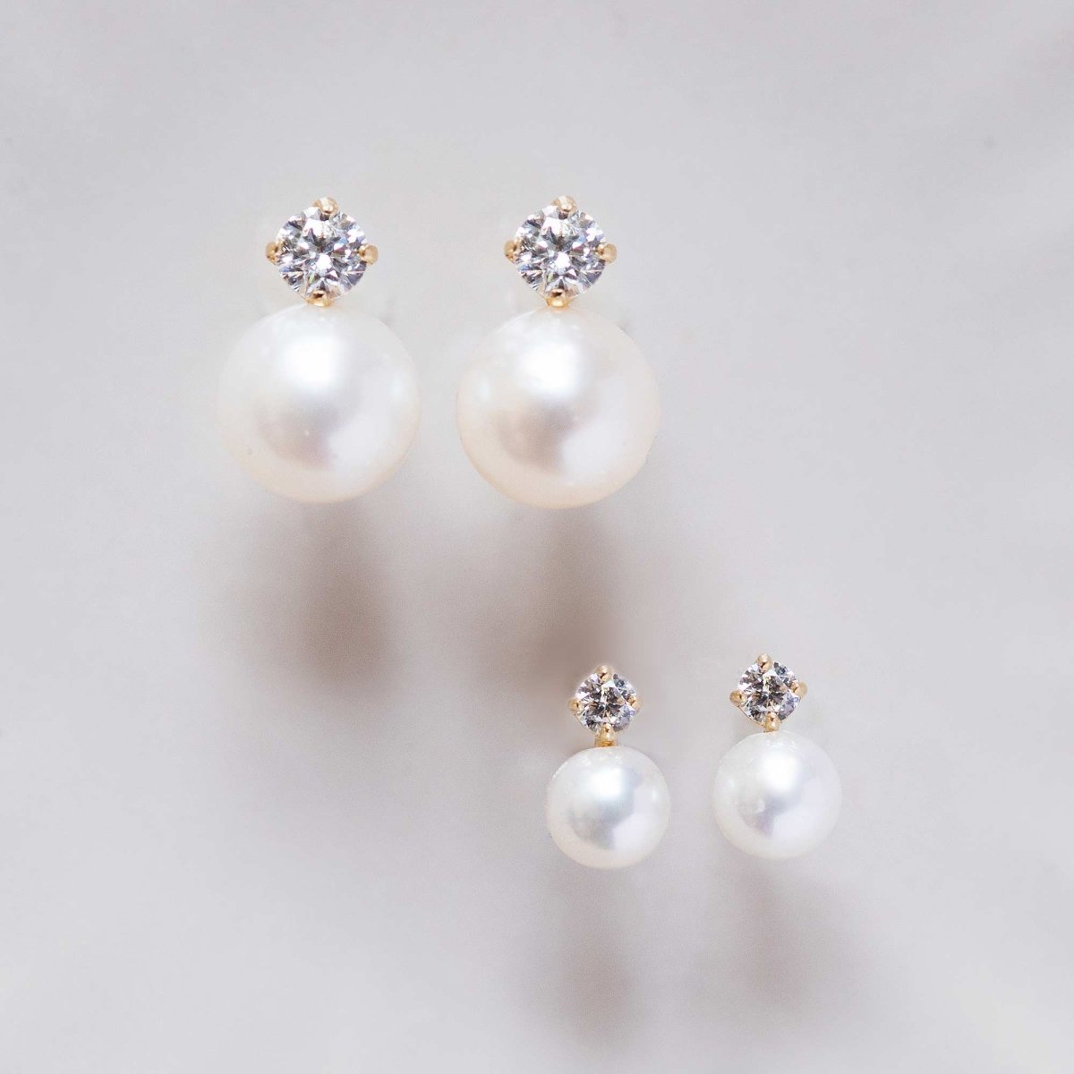 14K gold pearl and clear-stone studs in two sizes, shown together on a soft grey surface