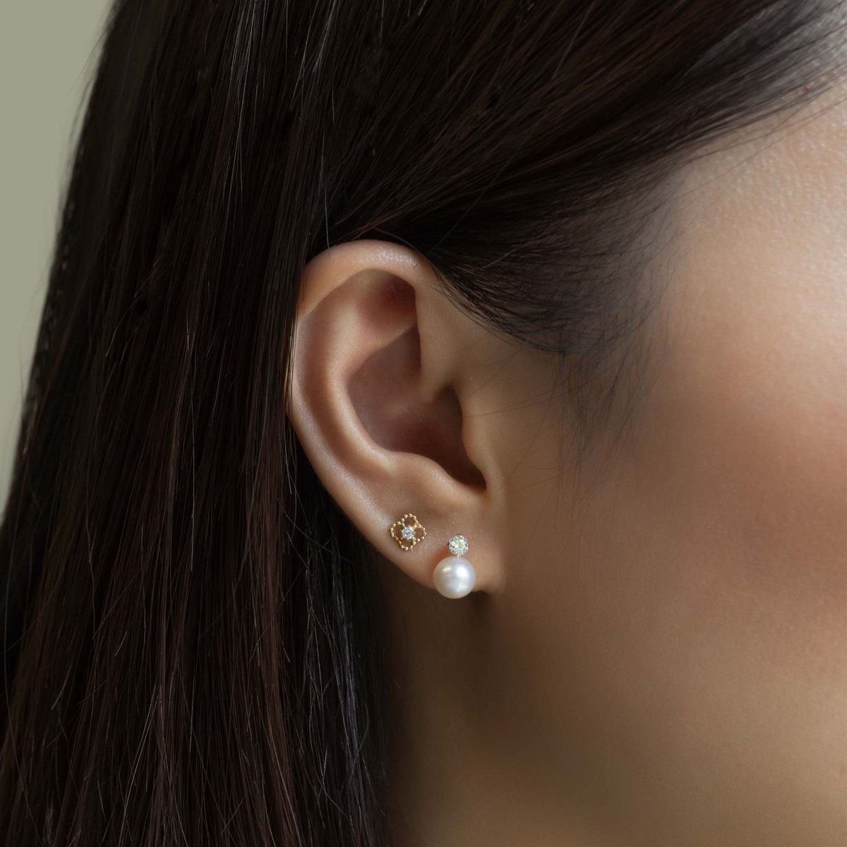 14K gold zirconia flora stud worn with a clear-stone stud and pearl stud on a model's lobe
