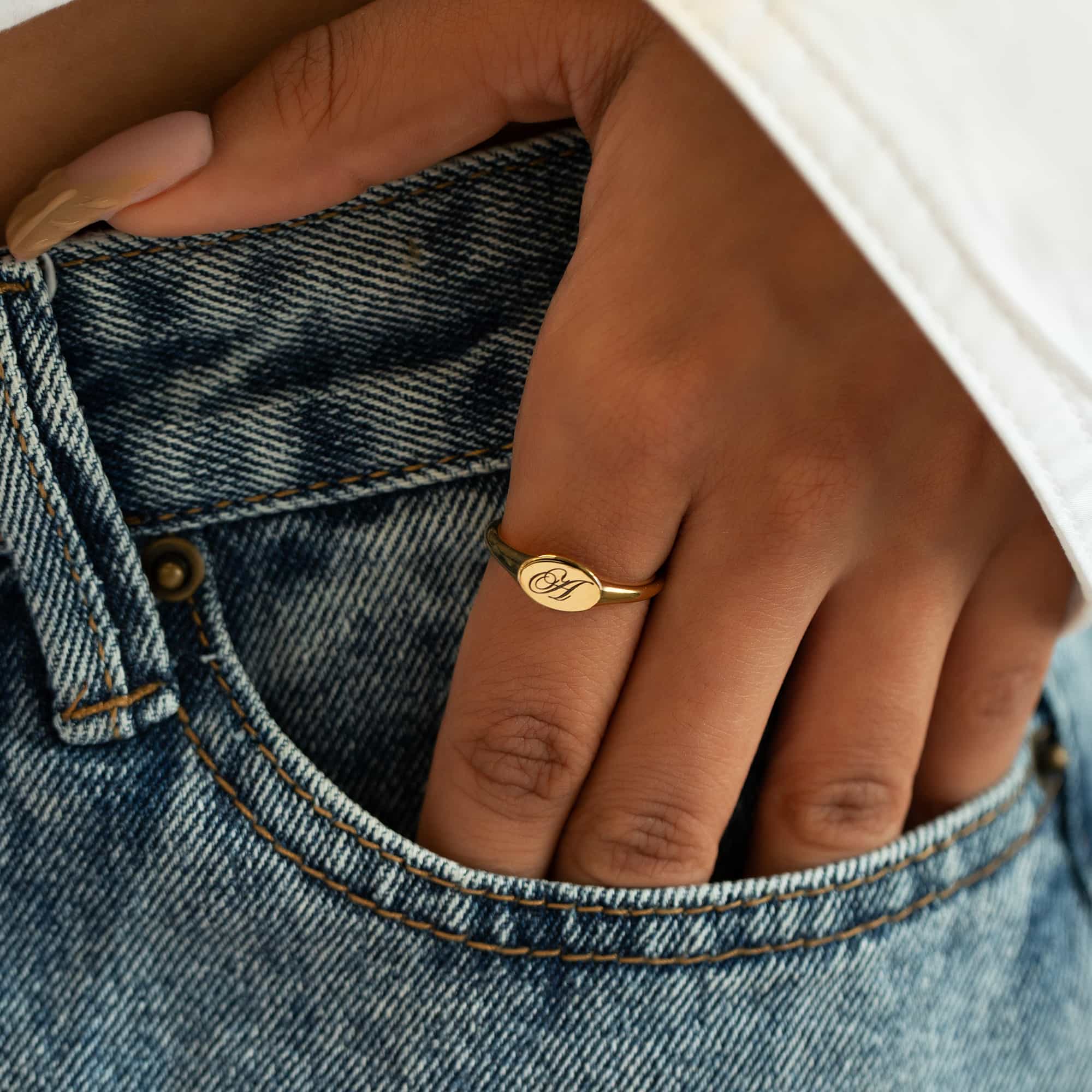 Gold vermeil oval signet ring engraved with an initial, shown on a hand tucked in a jeans pocket