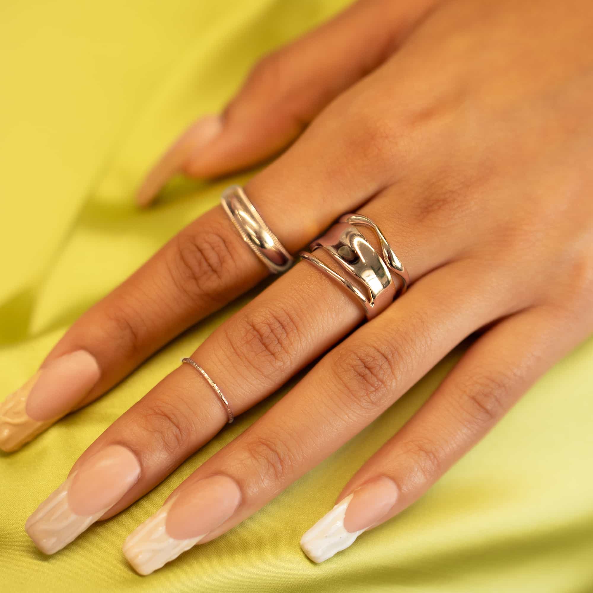 Silver wide band ring and milgrain band ring on a model's fingers over yellow fabric