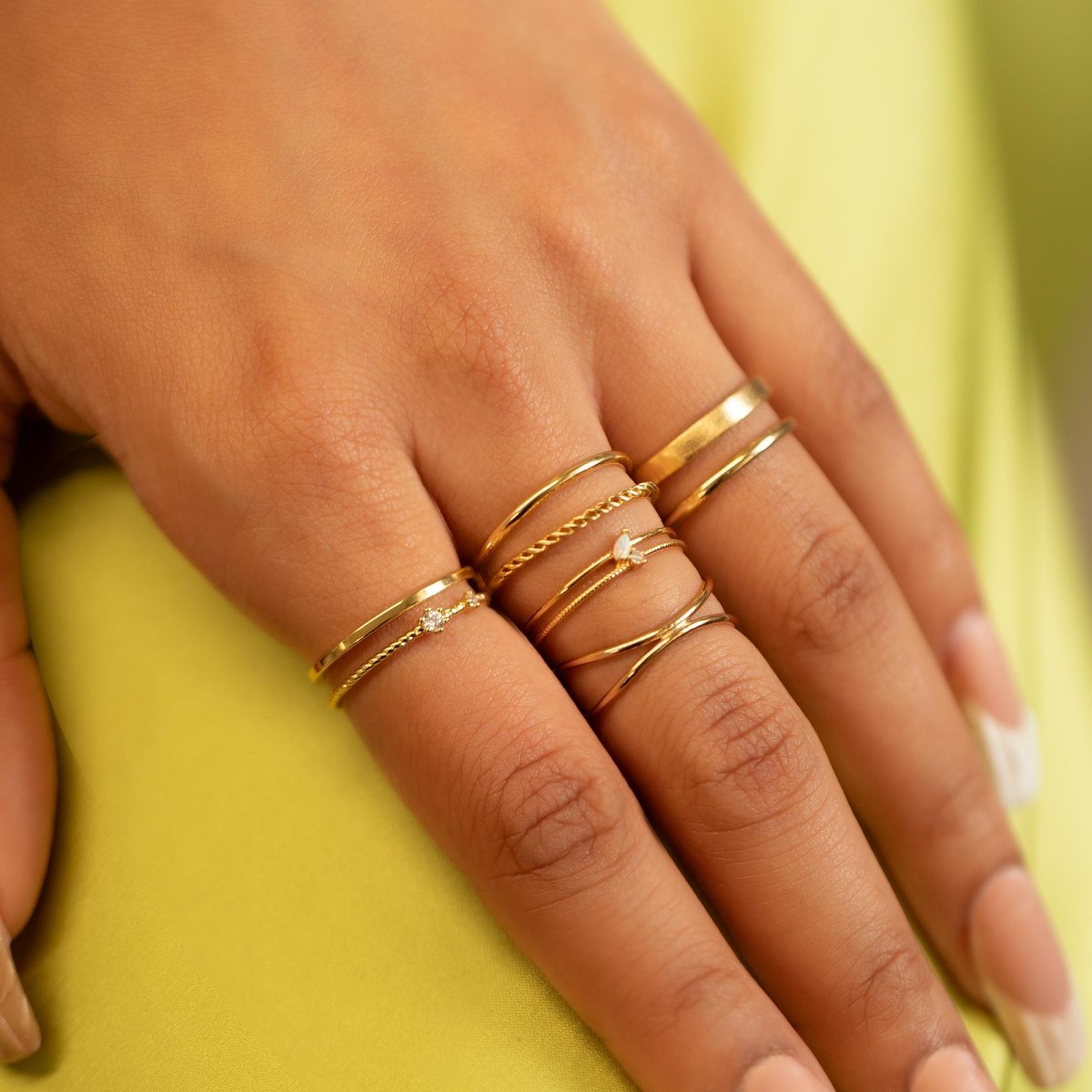 Gold thin stacking rings, including criss-cross and stone bands, worn across a model's fingers