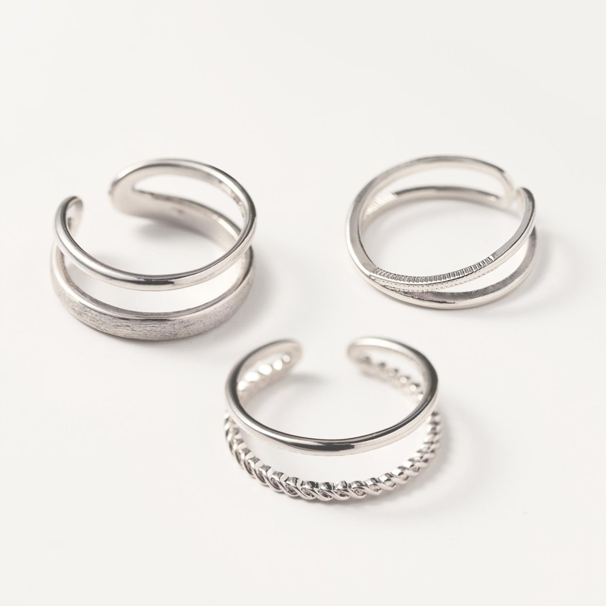 Three sterling silver open stacking rings including a rope-twist double-band design, on a cream background