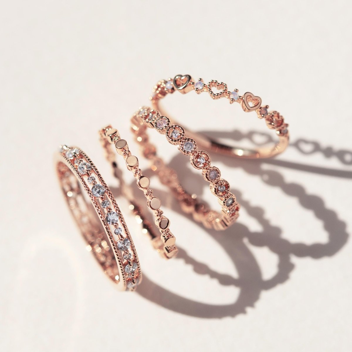 Rose gold vermeil flat beaded stacking ring set with heart and clear-stone bands, on a cream background