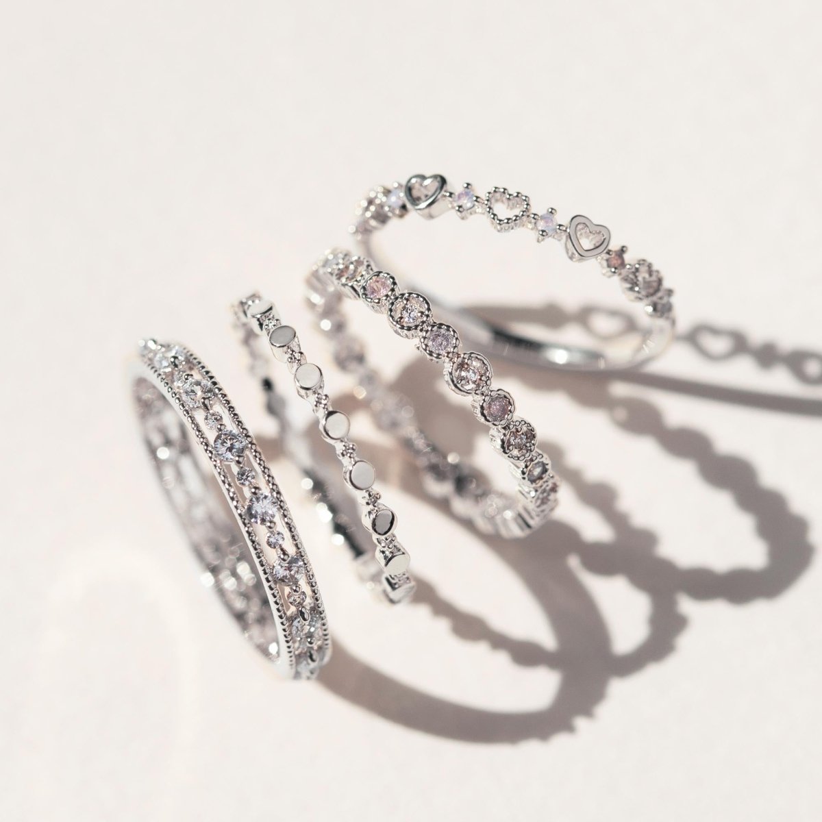 Sterling silver eternity stacking rings with clear white zirconia stones, stacked on a cream surface