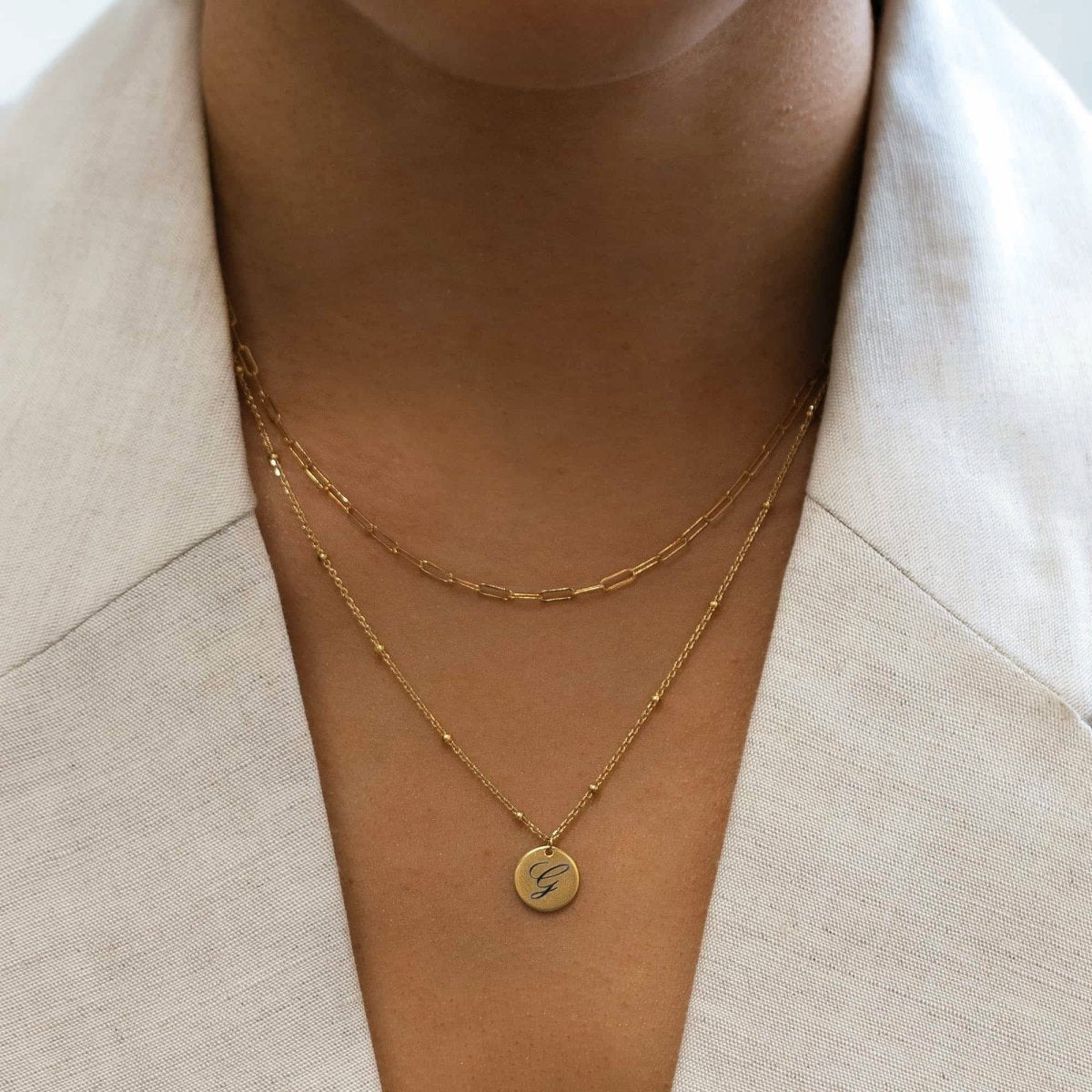 Gold-filled paperclip chain necklace layered with an engraved initial disc necklace on a model