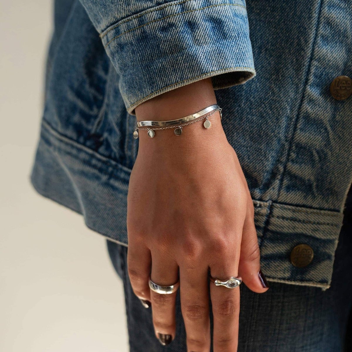 Sterling silver herringbone chain bracelet with dangling charms, shown on a model's wrist