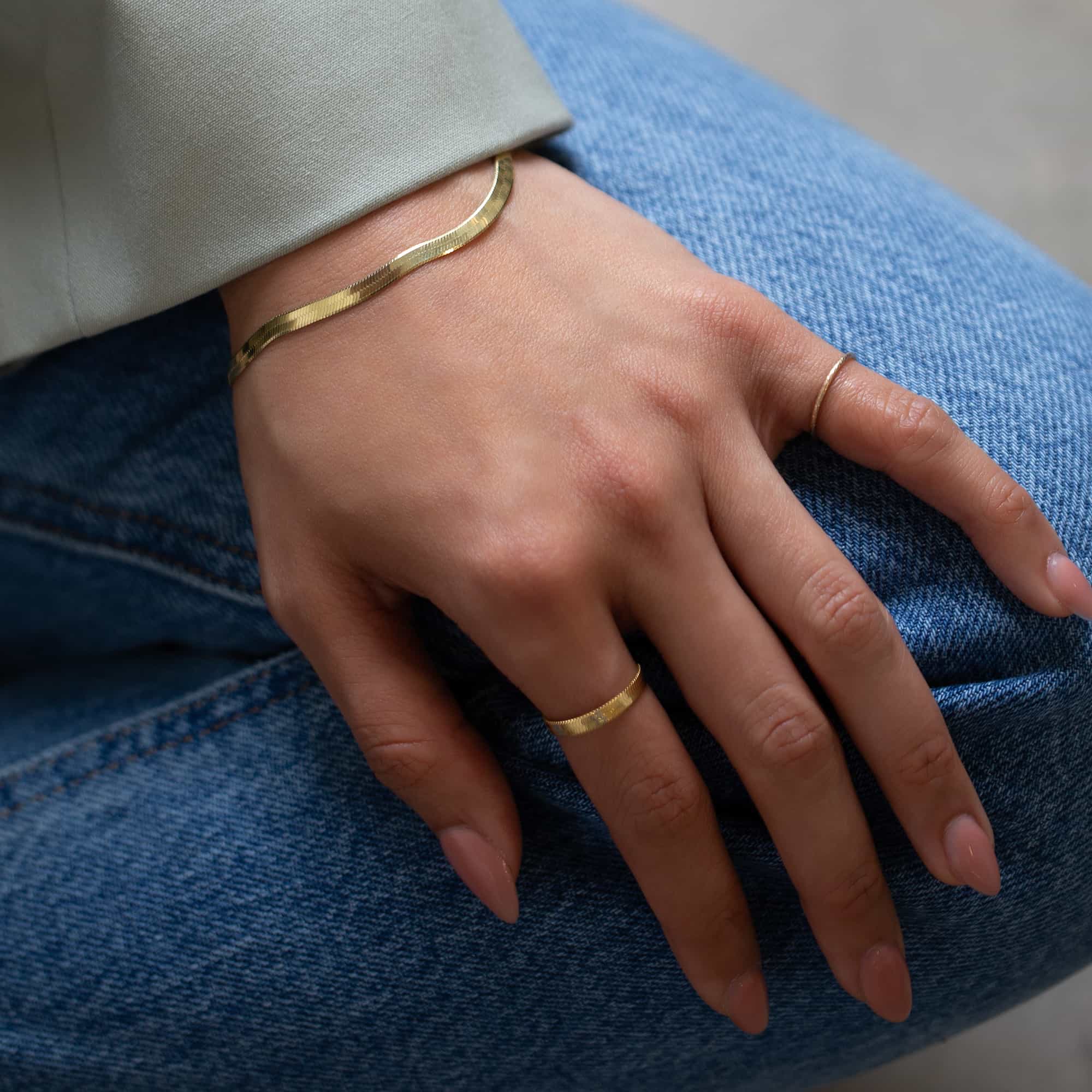 Gold vermeil herringbone chain stacking ring shown on a model's finger resting on denim