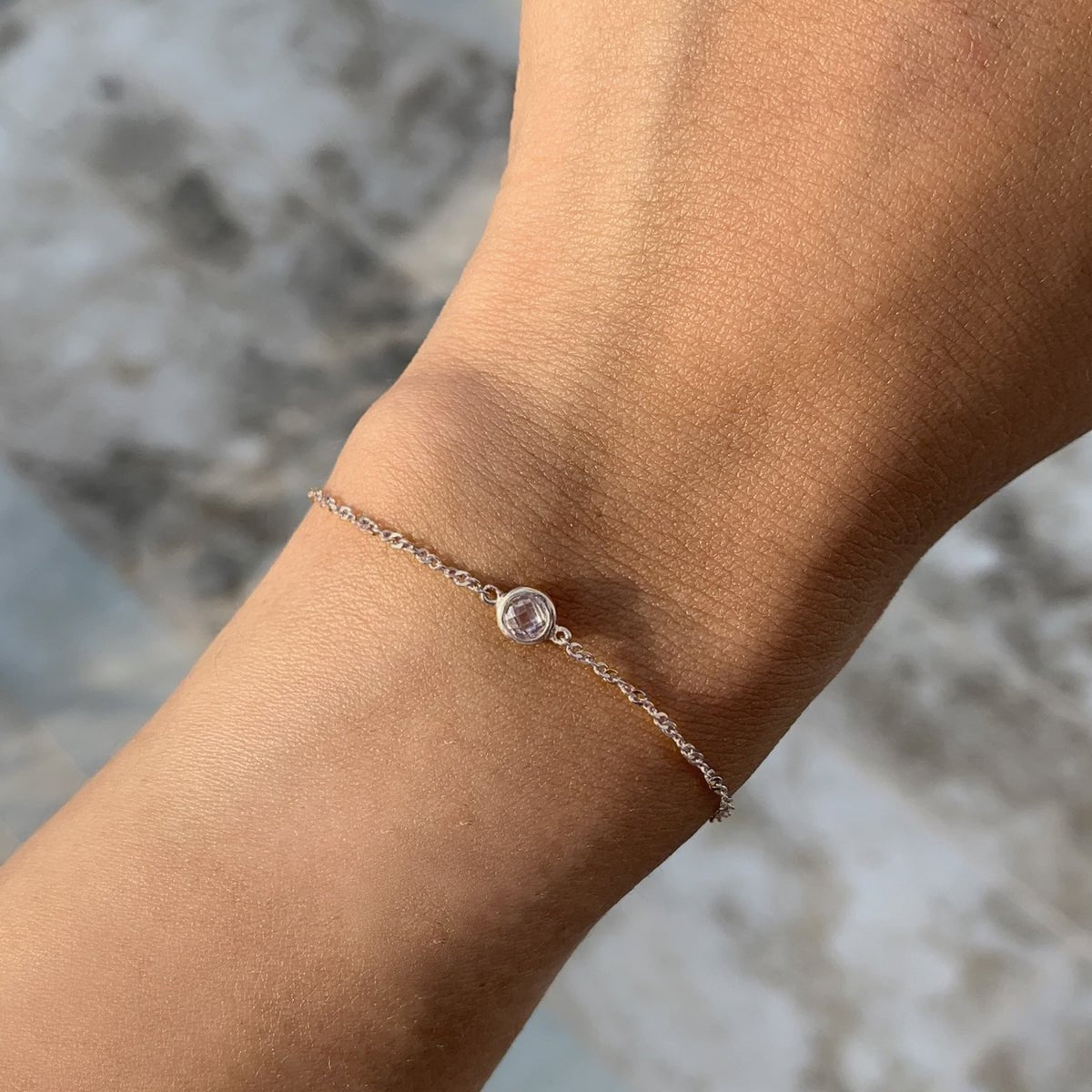 Sterling silver Singapore chain bracelet with a clear bezel stone, shown on a model's wrist