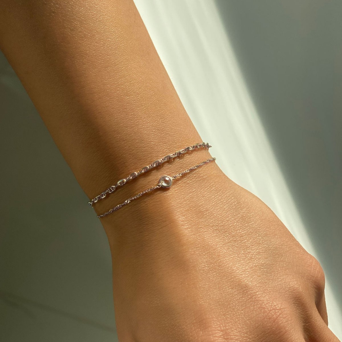 Sterling silver thin chain bracelet with a single bezel-set clear stone, shown on a wrist