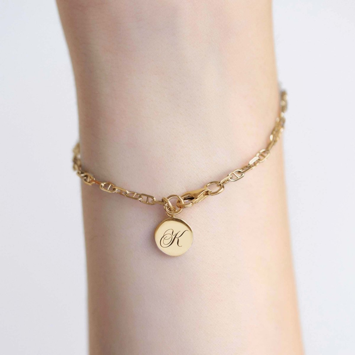 Gold Marina chain bracelet with an engraved round initial charm, shown on a model's wrist