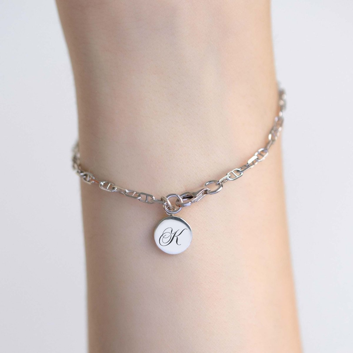 Silver Marina chain bracelet with an engraved round initial charm, shown on a model's wrist