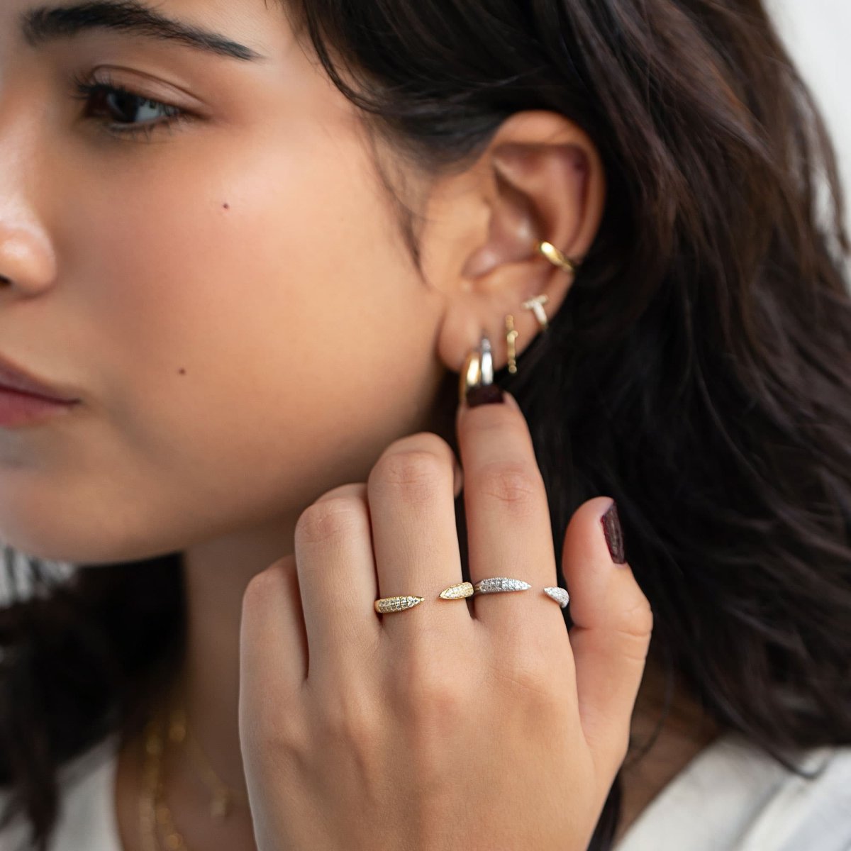 Sterling silver claw pave rings with white zirconia spikes shown on a model's fingers near her ear