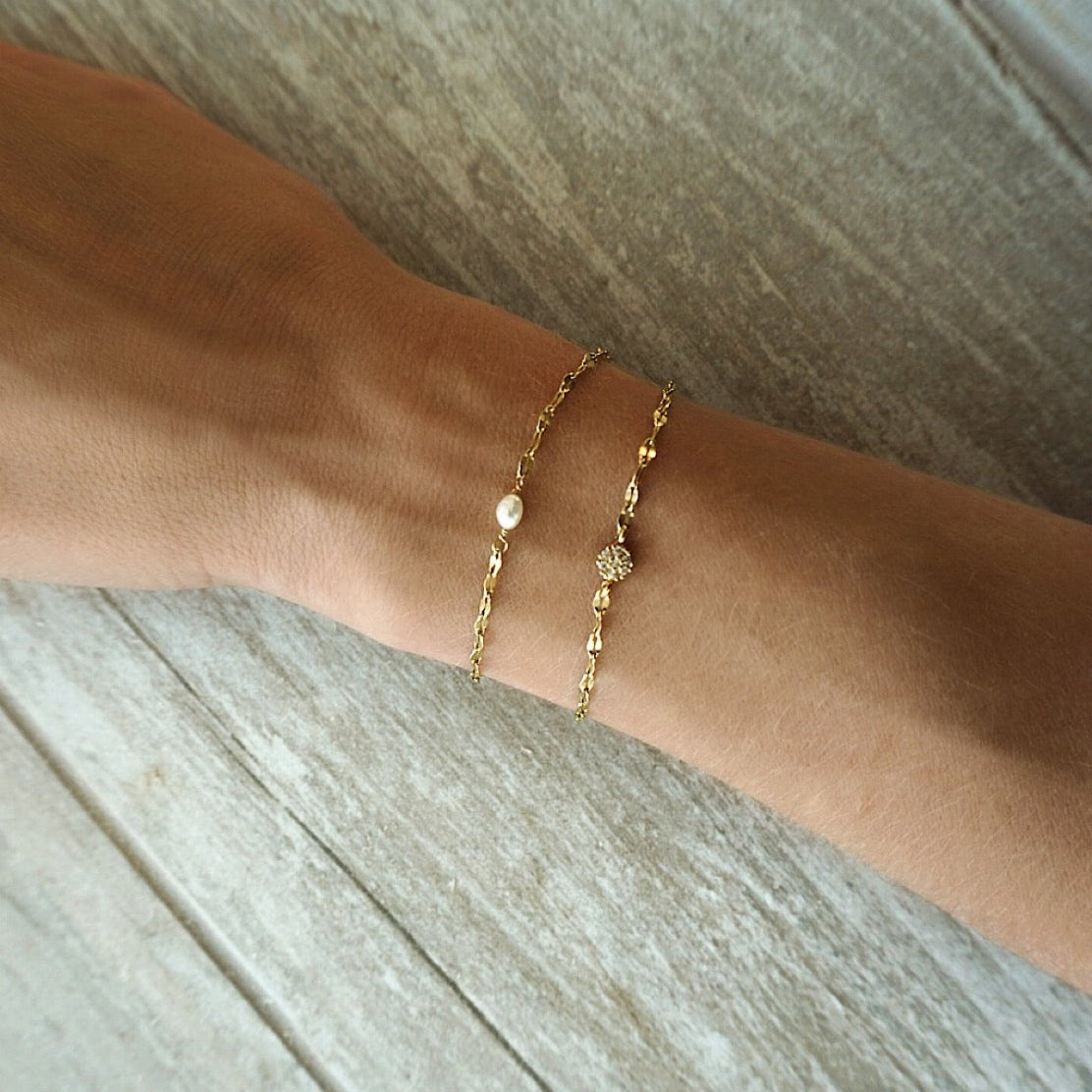 Gold vermeil mirror-link pearl bracelet layered with a thin chain, shown on a wrist on weathered wood