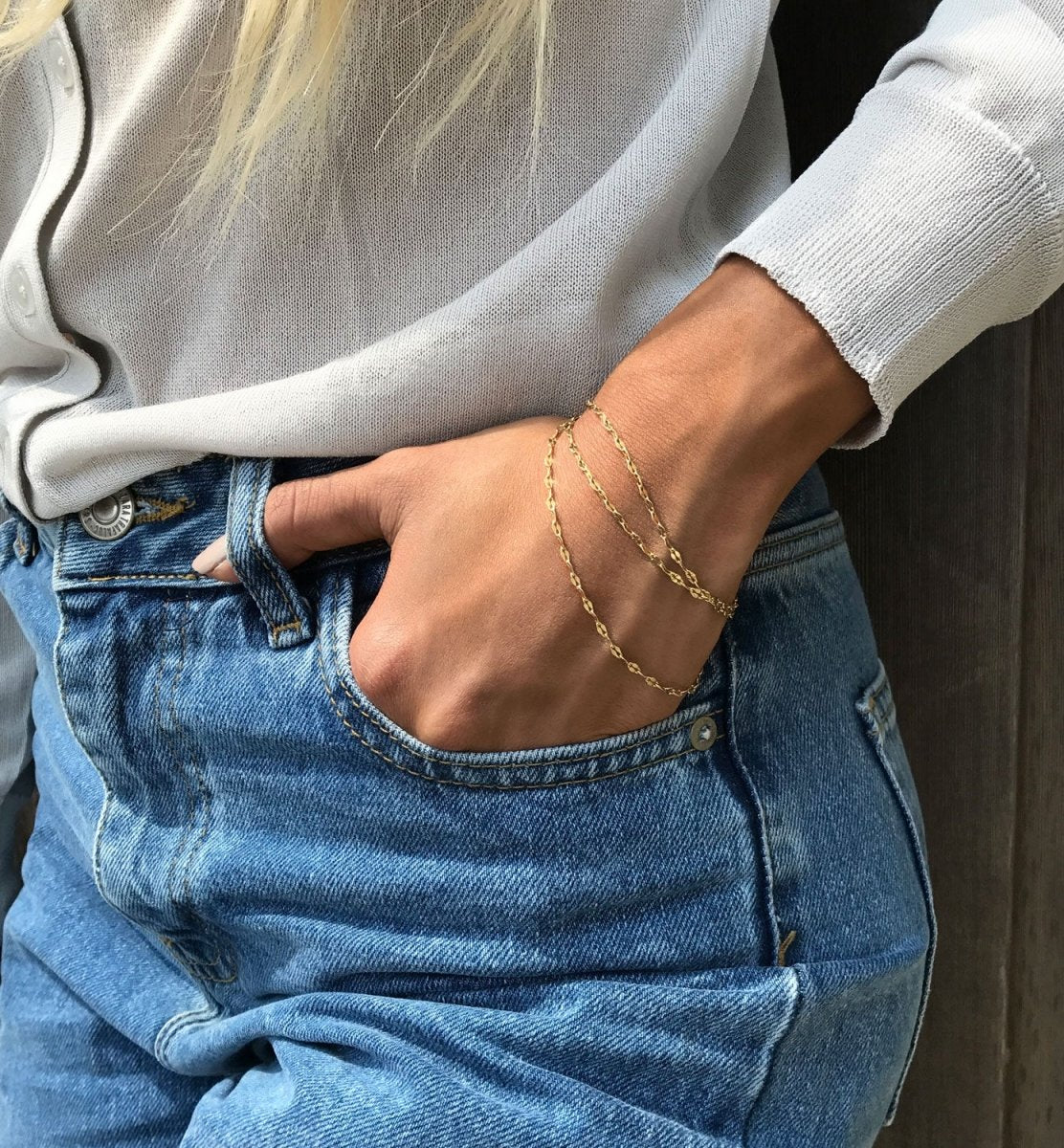 Gold vermeil layered chain bracelet set shown on a model's wrist tucked into jeans