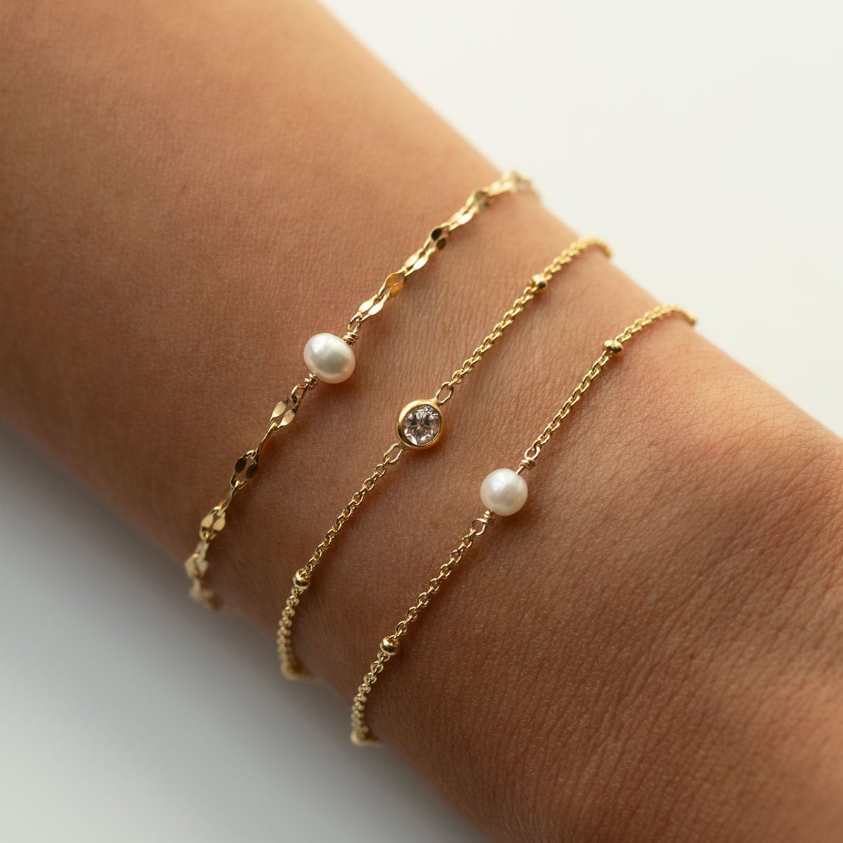 Gold vermeil mirror-link pearl bracelet stacked with two thin gold chains, shown on a wrist