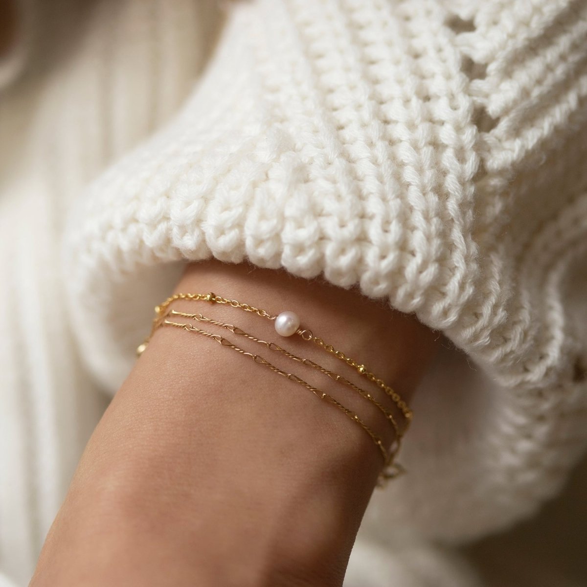 Rose gold vermeil chain bracelet with a single pearl, layered with thin chains on a model's wrist