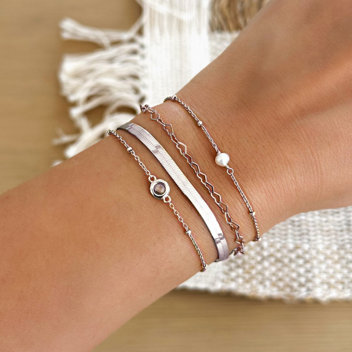 Silver herringbone, beaded, pearl and stone chain bracelets stacked on a model's wrist