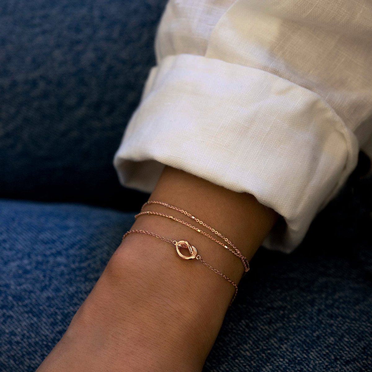Rose gold vermeil love knot bracelet shown on a model's wrist with a white cuff and denim