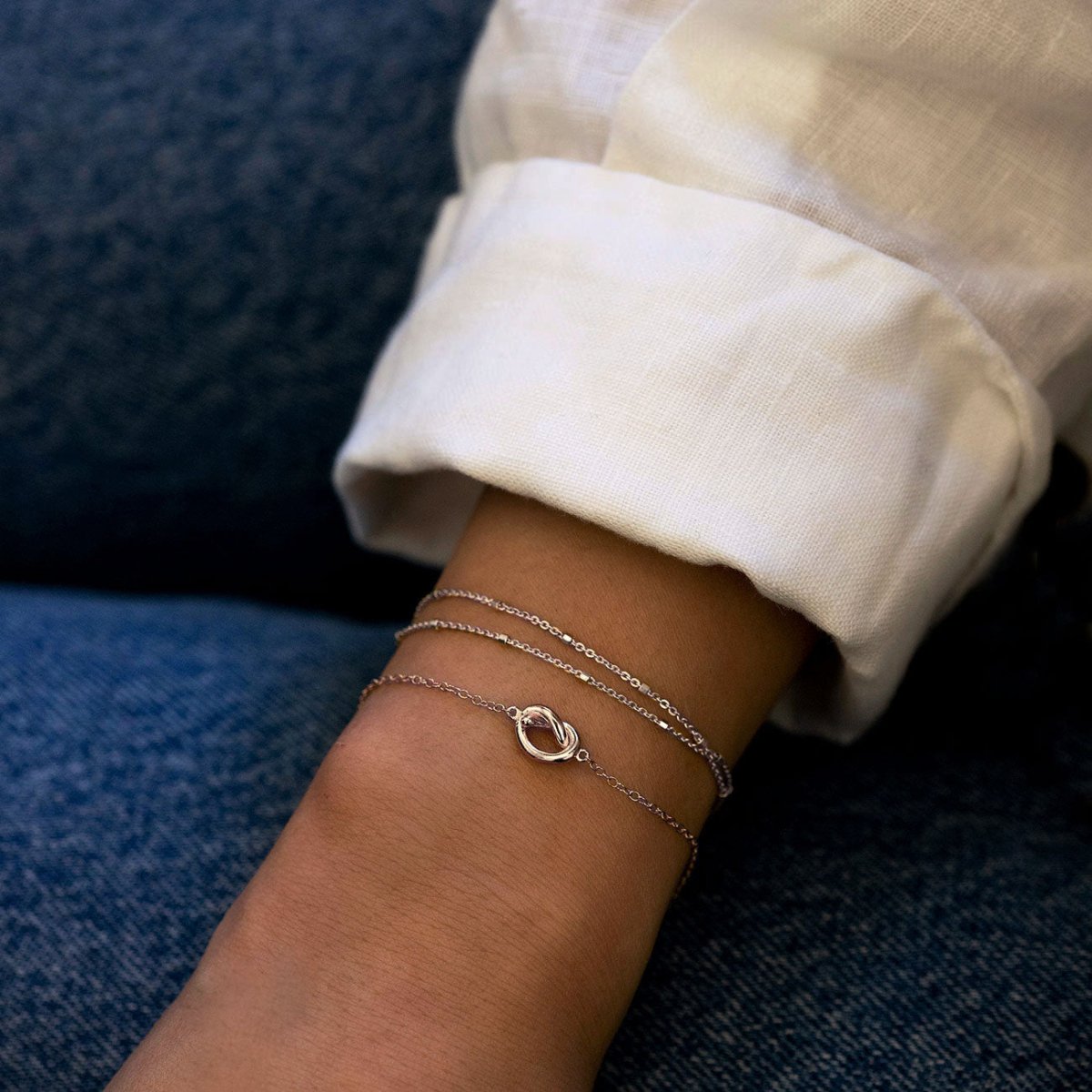 Sterling silver layered chain bracelet with a twisted knot charm, shown on a model's wrist