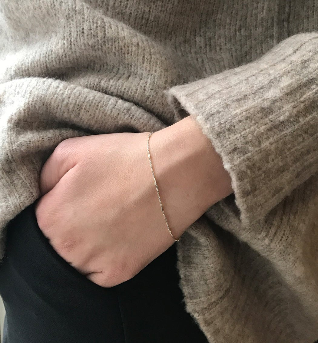 Sterling silver dainty thin chain bracelet, shown on a model's wrist over a knit sweater