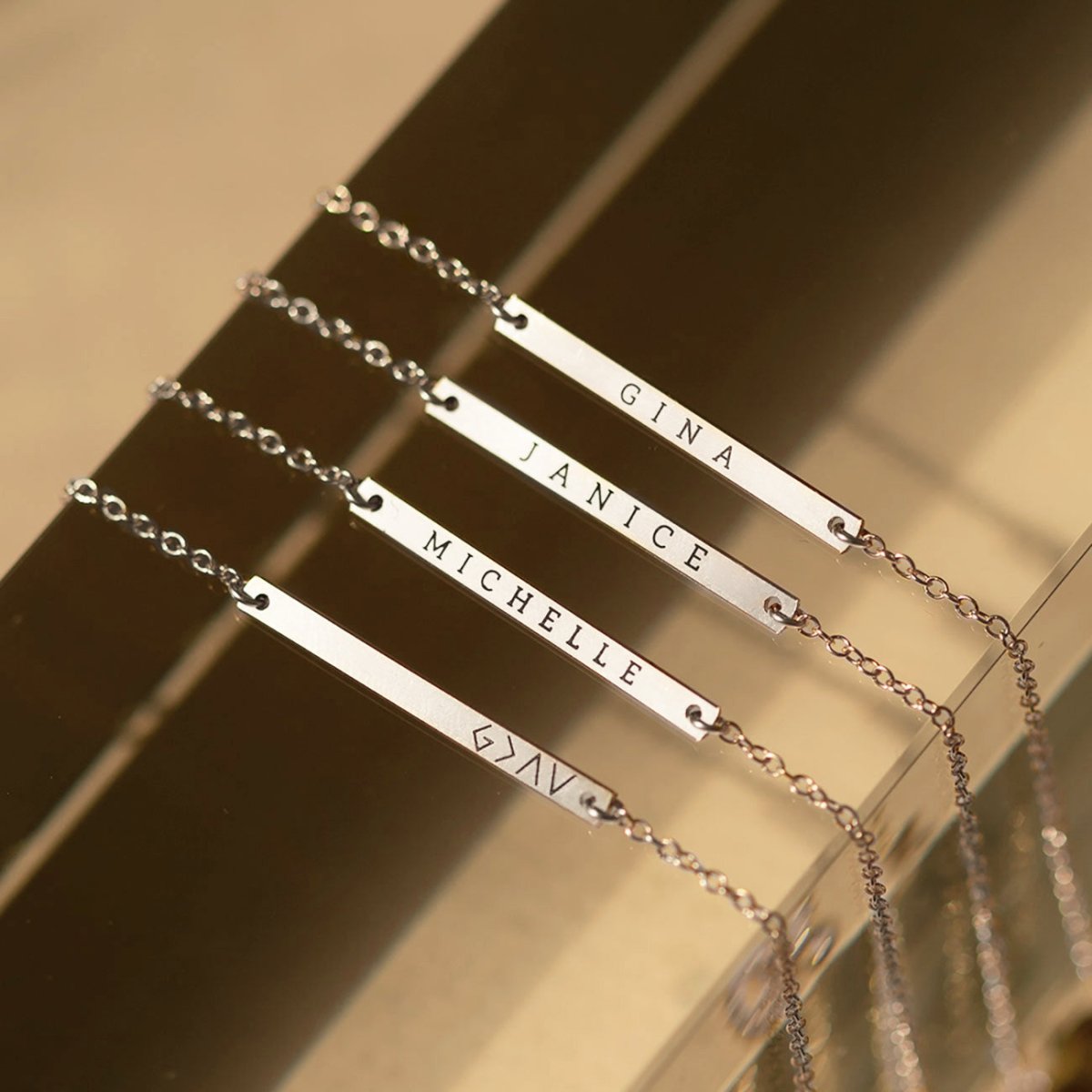 Four sterling silver thin bar ID bracelets engraved with names and a symbol, lined up on a mirrored surface