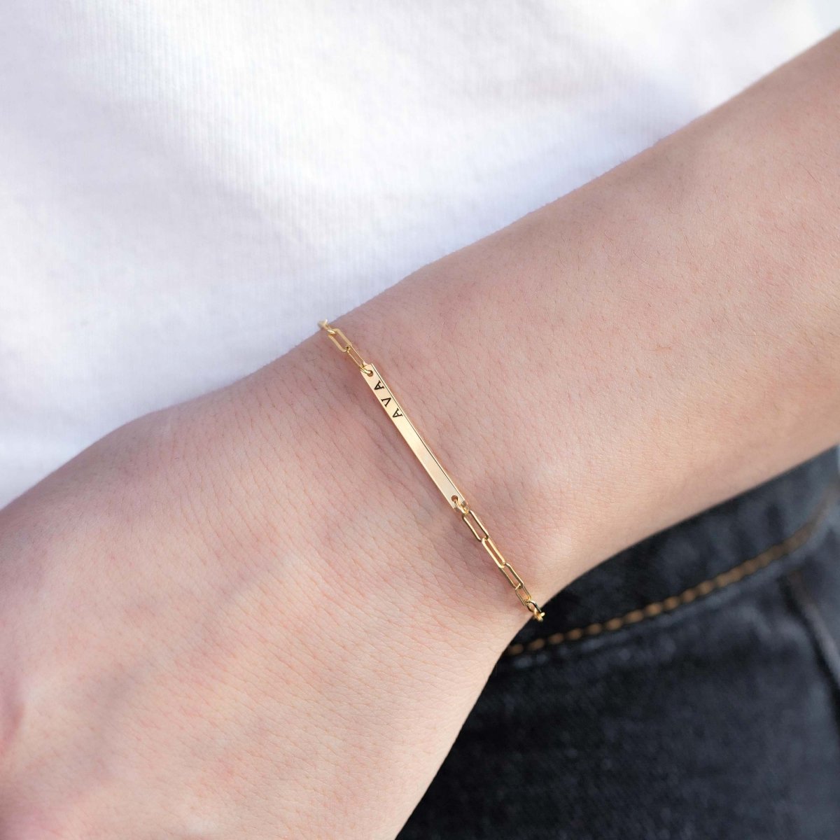 Gold-filled thin bar paperclip chain bracelet engraved with a name, close-up on a model's wrist