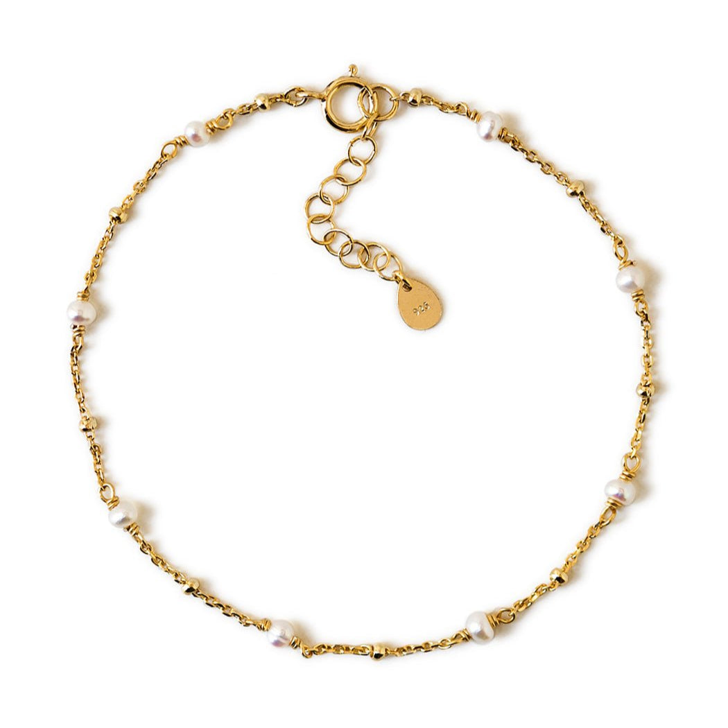 Gold vermeil satellite chain bracelet with small white pearls, laid on a white background