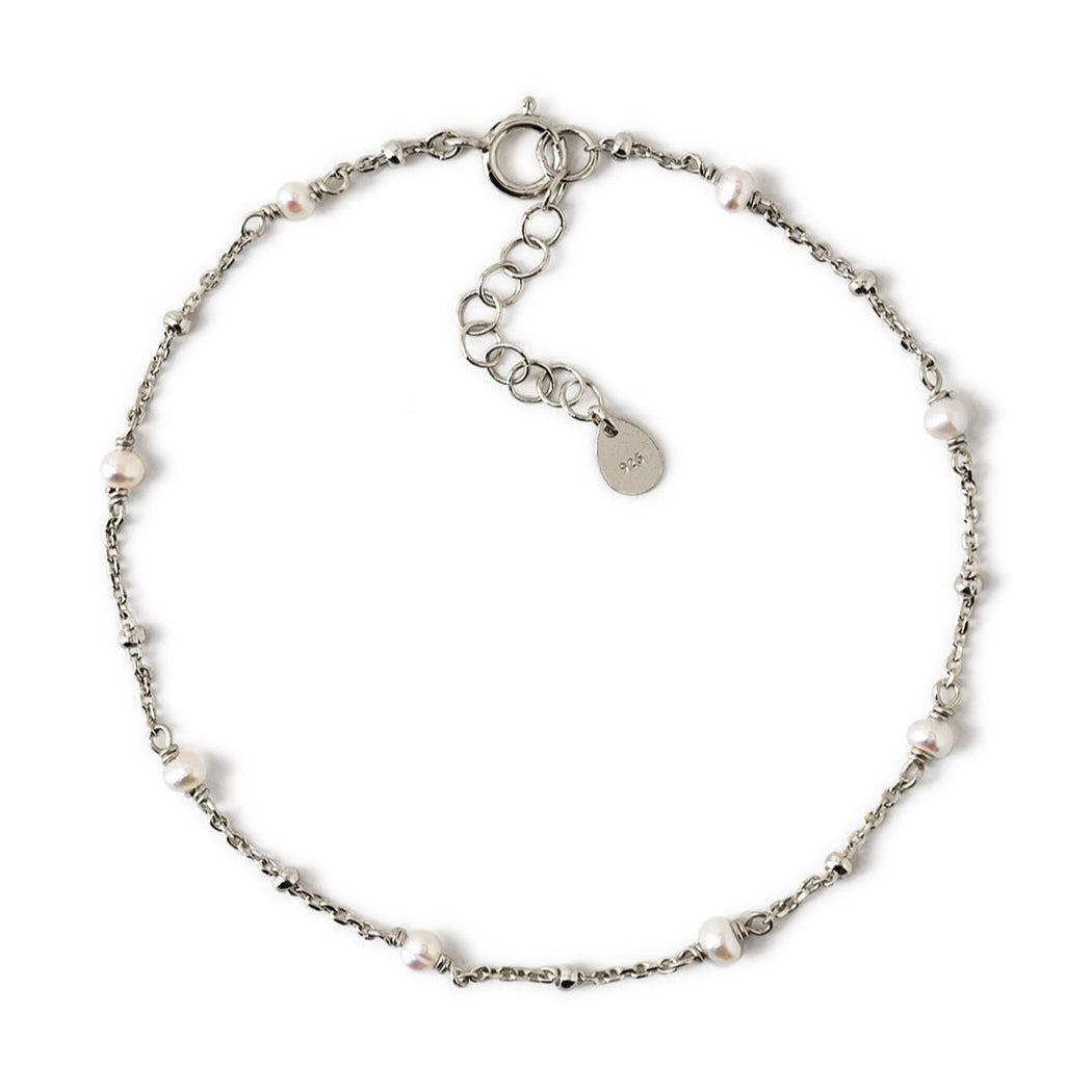 Sterling silver satellite chain bracelet with small white pearls, laid on a white background