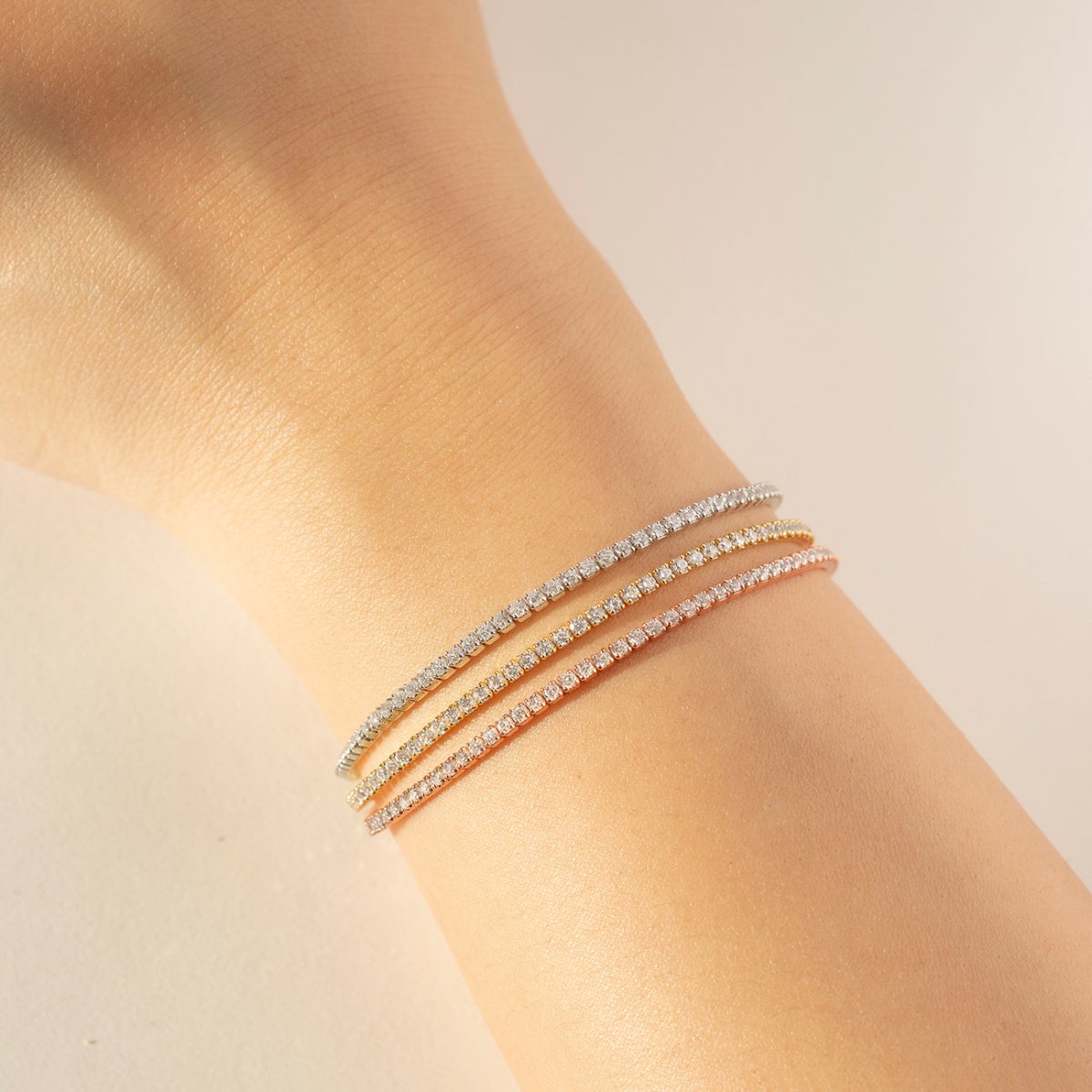 Three thin crystal line bracelets in silver, gold and rose gold tones, stacked on a model's wrist