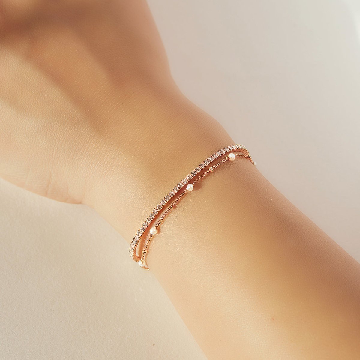 Rose gold vermeil pearl chain layered with a clear-stone tennis bracelet, shown on a wrist