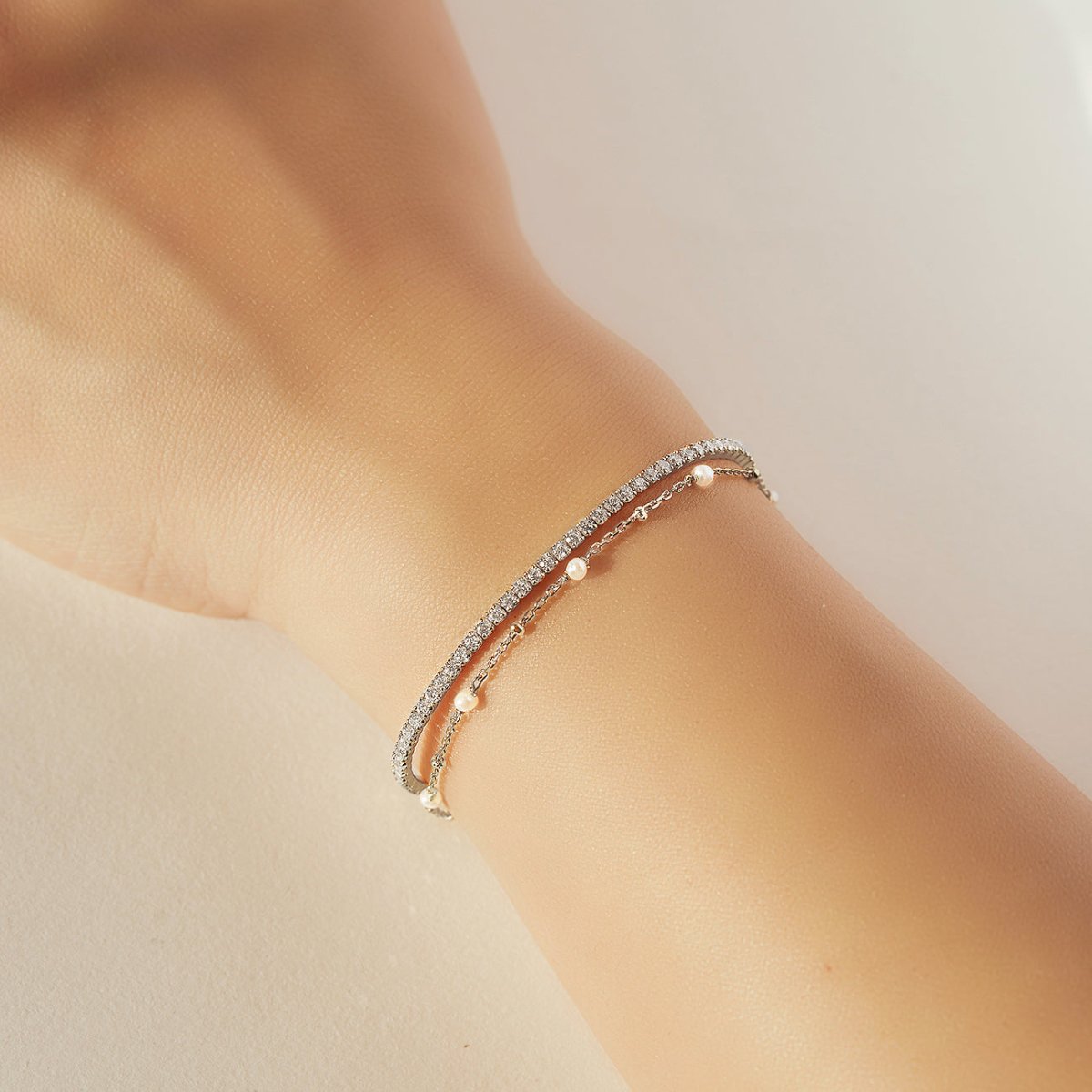 Sterling silver crystal line bracelet with white zirconia, layered with a pearl chain on a model's wrist