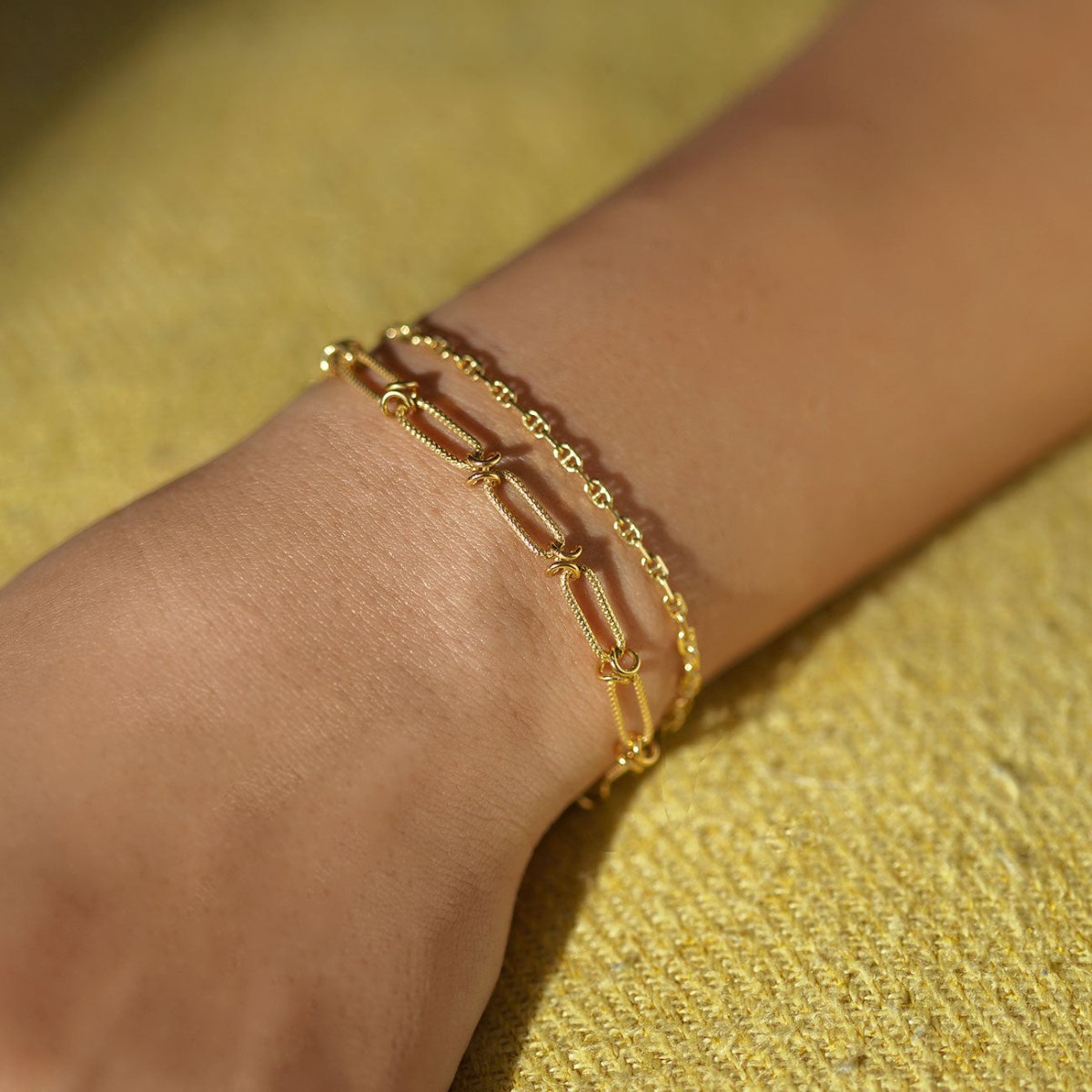 Gold vermeil chain link bracelet stacked on a wrist against a yellow fabric backdrop