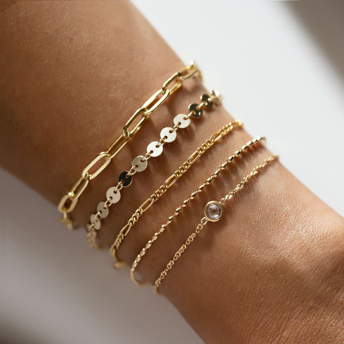 Gold vermeil Singapore chain bracelet with a clear bezel stone, styled in a wrist stack