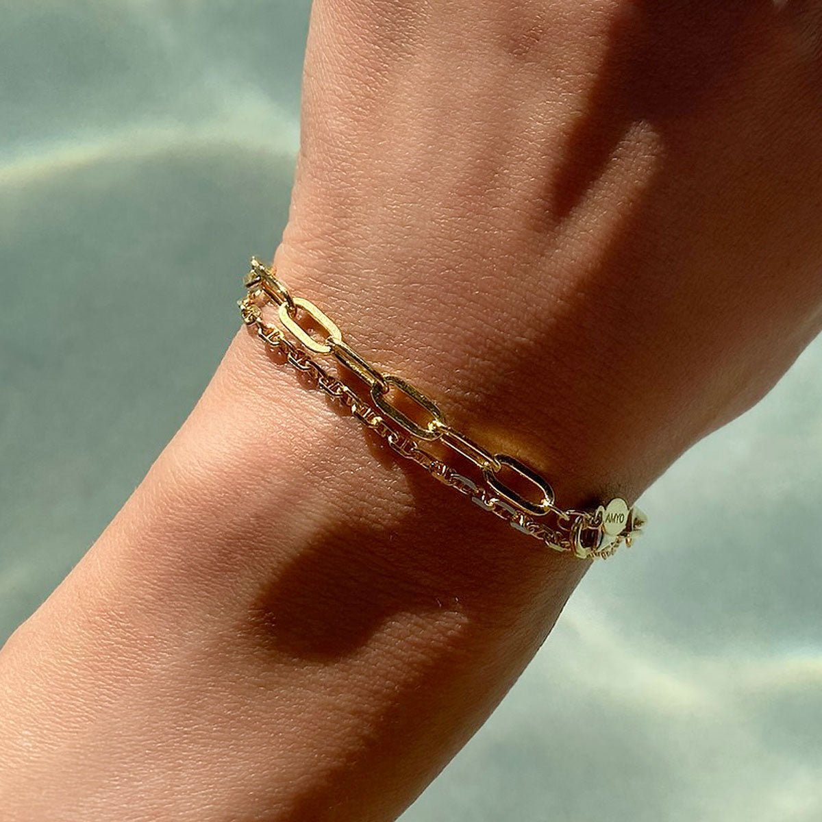 14K gold Marina chain bracelet layered with a paperclip chain, shown on a model's wrist