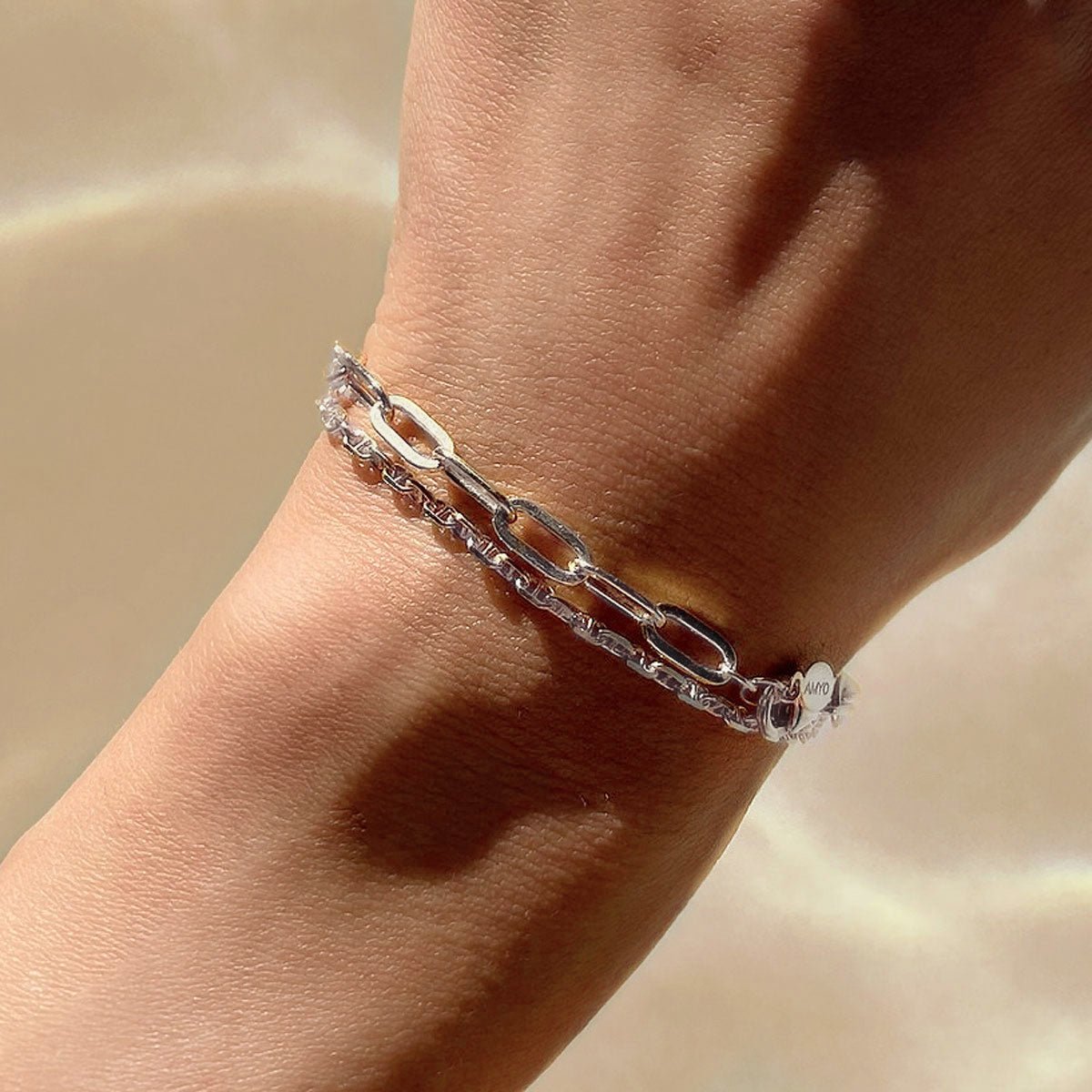 Sterling silver paperclip chain bracelet layered with a finer chain on a model's wrist