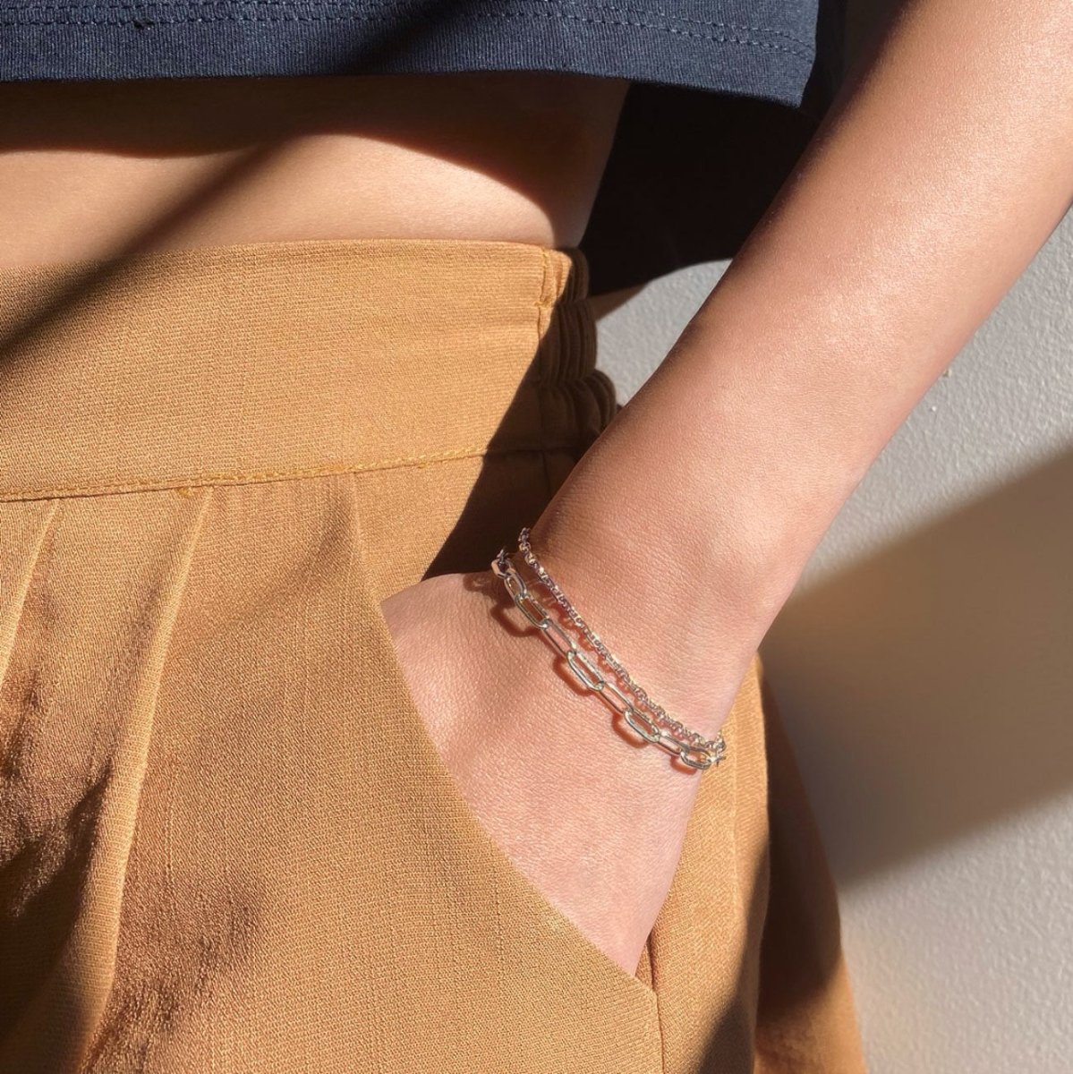 Sterling silver paperclip chain bracelet layered on a wrist tucked into a tan pocket