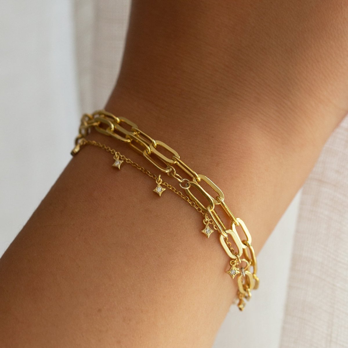 Gold vermeil star dangle bracelet shown stacked with other gold chain bracelets on a model's wrist