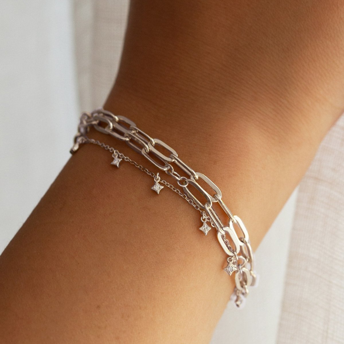 Sterling silver star dangle bracelet layered with a silver paperclip chain, shown on a model's wrist