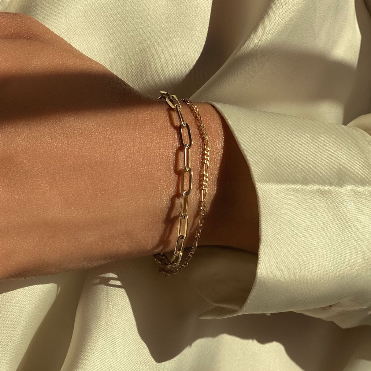 14K gold Figaro chain bracelet stacked with a paperclip chain, shown on a model's wrist