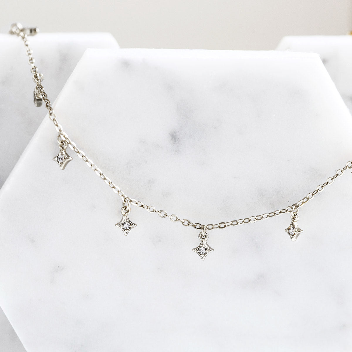 Sterling silver dangle bracelet with white zirconia star charms, close-up detail on white marble