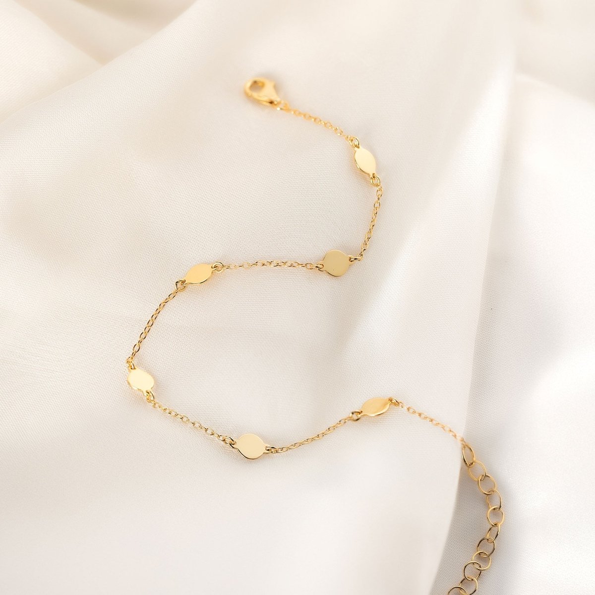 Gold vermeil round disc station bracelet curved on cream fabric, shown loose