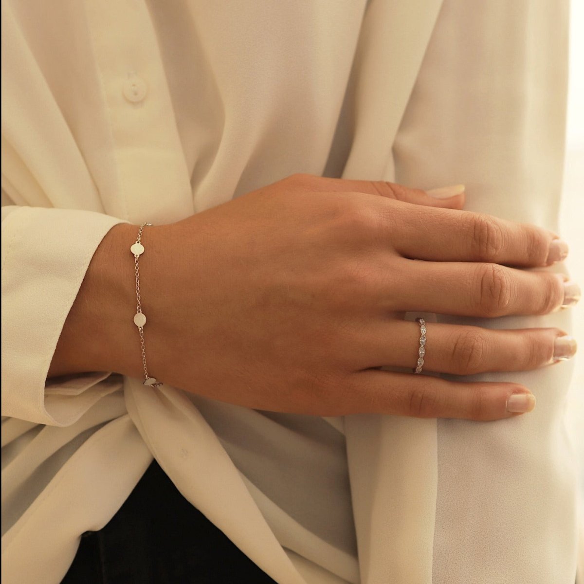 Sterling silver round disc station bracelet shown on a model's wrist with a ring and blouse