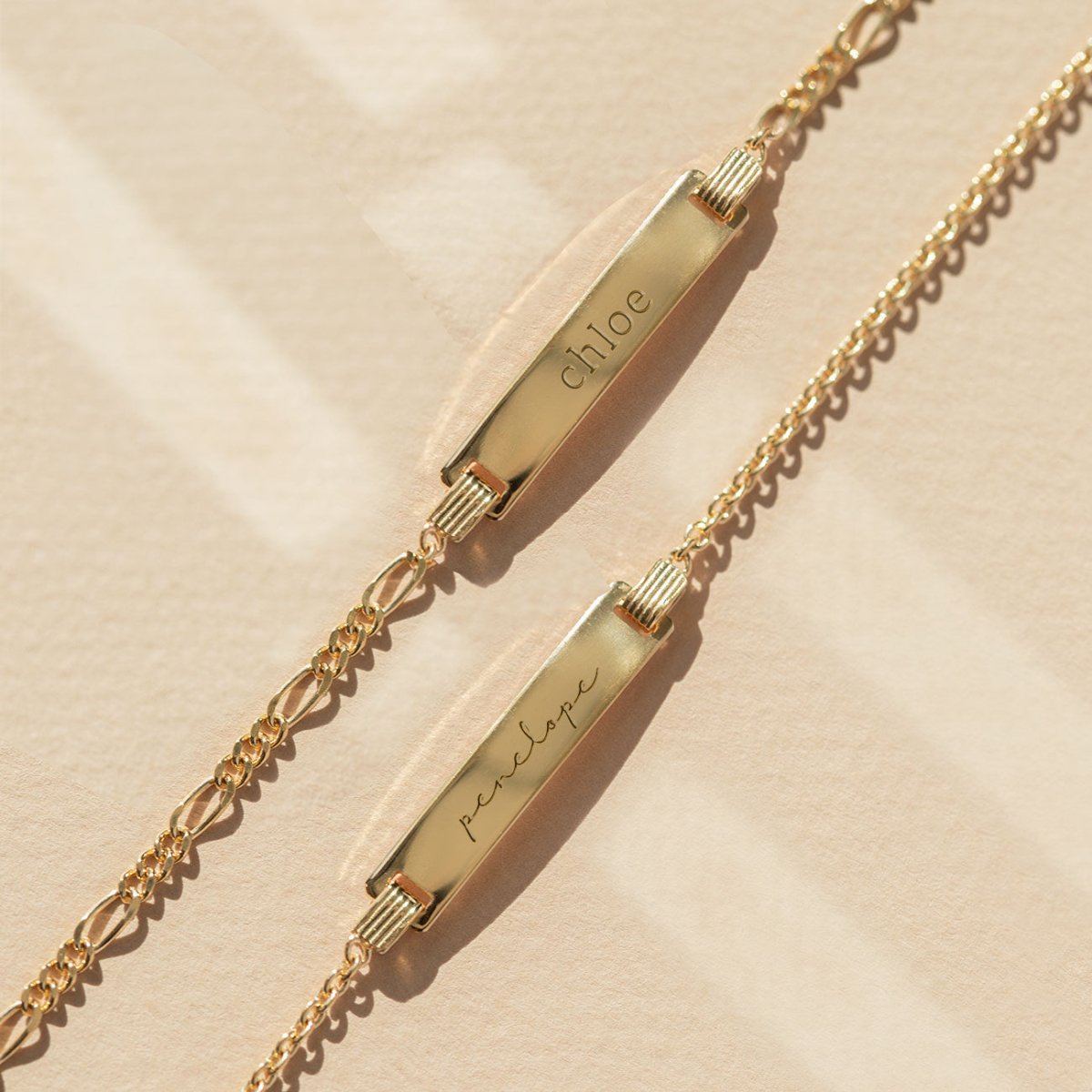 Gold vermeil Figaro chain ID bracelets engraved with names, laid on a warm neutral surface