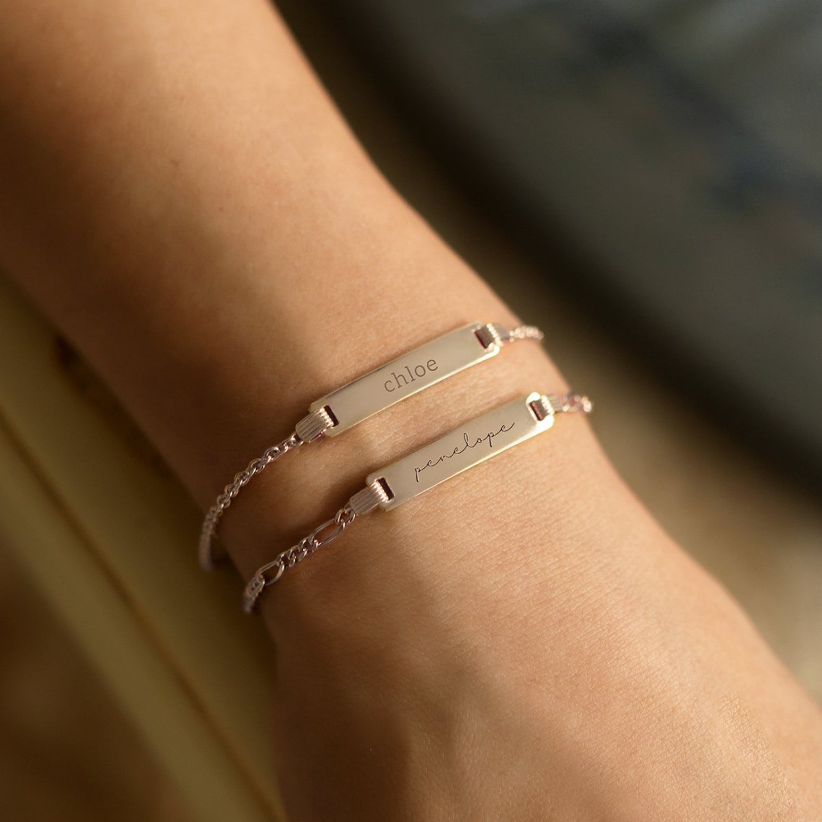 Sterling silver Figaro chain ID bracelets, each engraved with a name, on a model's wrist