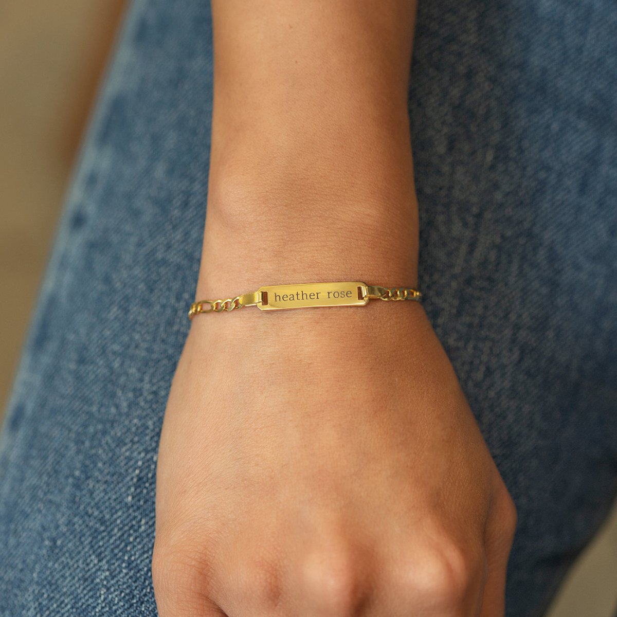 Gold vermeil Figaro chain ID bracelet engraved with a name, shown on a model's wrist
