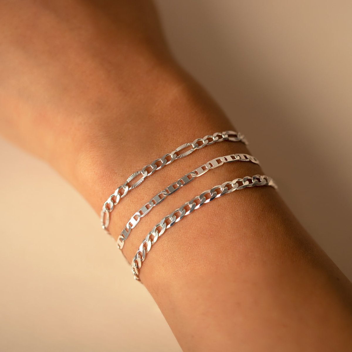Sterling silver faceted Figaro chain bracelet close-up, stacked with two more chains on a wrist