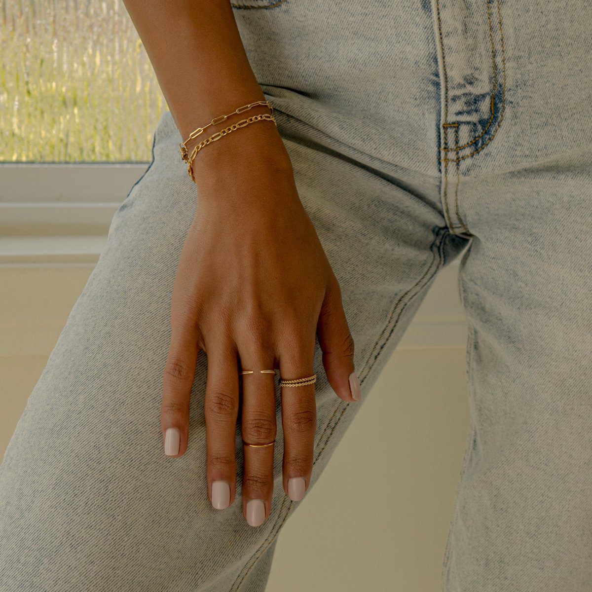 Gold vermeil faceted Figaro chain bracelet shown on a model's wrist resting on jeans