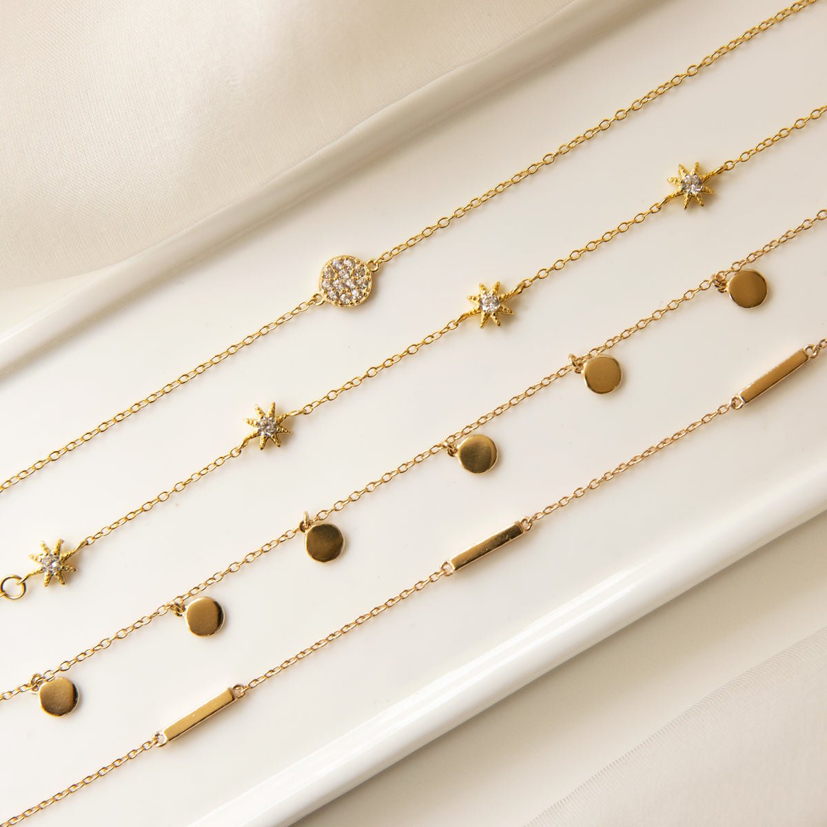 Gold vermeil disc dangle bracelet shown layered with other charm chains, on a cream background
