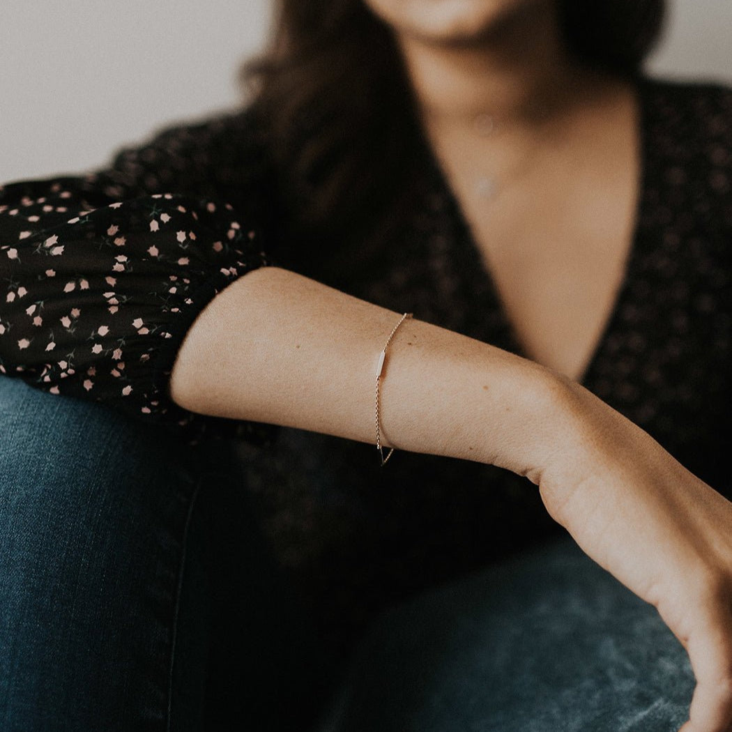 Rose gold vermeil eternity bar bracelet on a fine chain, shown on a seated model's wrist