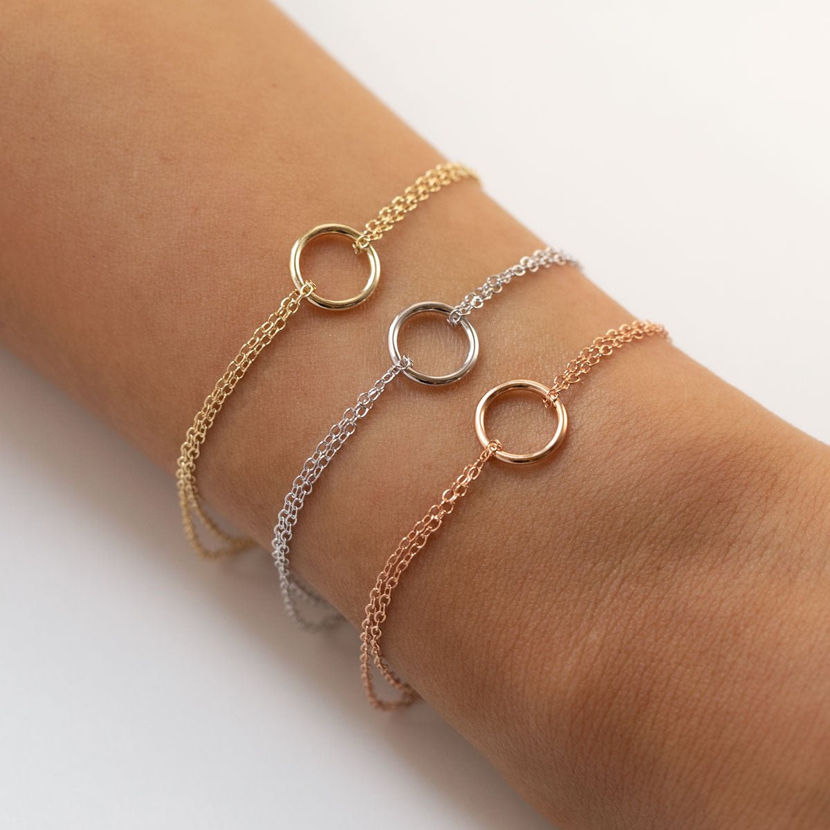 Gold, silver and rose gold eternity circle bracelets layered on a model's wrist